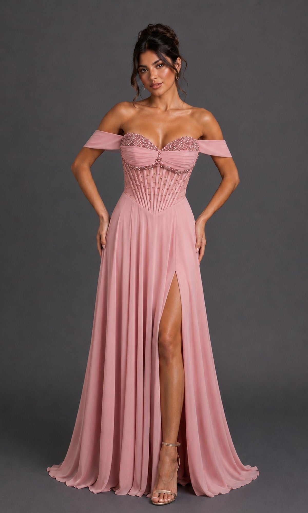 A woman wears the Long Prom Dress: Dancing Queen 4615 in blush, showcasing its off-the-shoulder neckline, embellished corset bodice, and a flowing a-line skirt with a high slit, standing gracefully against a plain dark background.